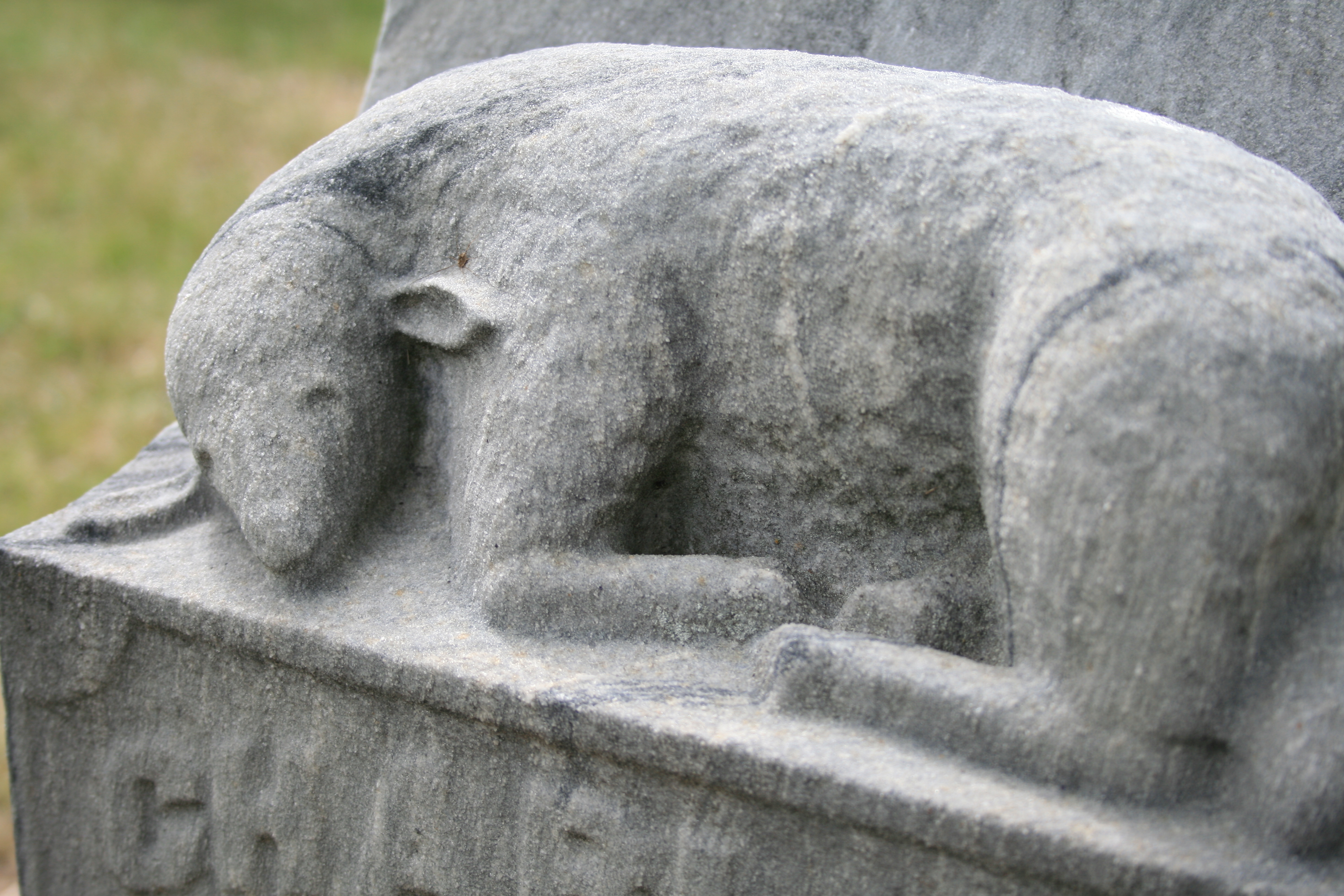 A stone lamb laying down on top of a tombstone